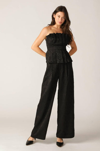 Woman wearing a black strapless top and wide-leg pants on a light background
