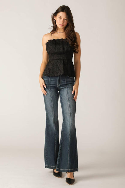 Woman wearing a black peplum top and blue jeans on a plain background