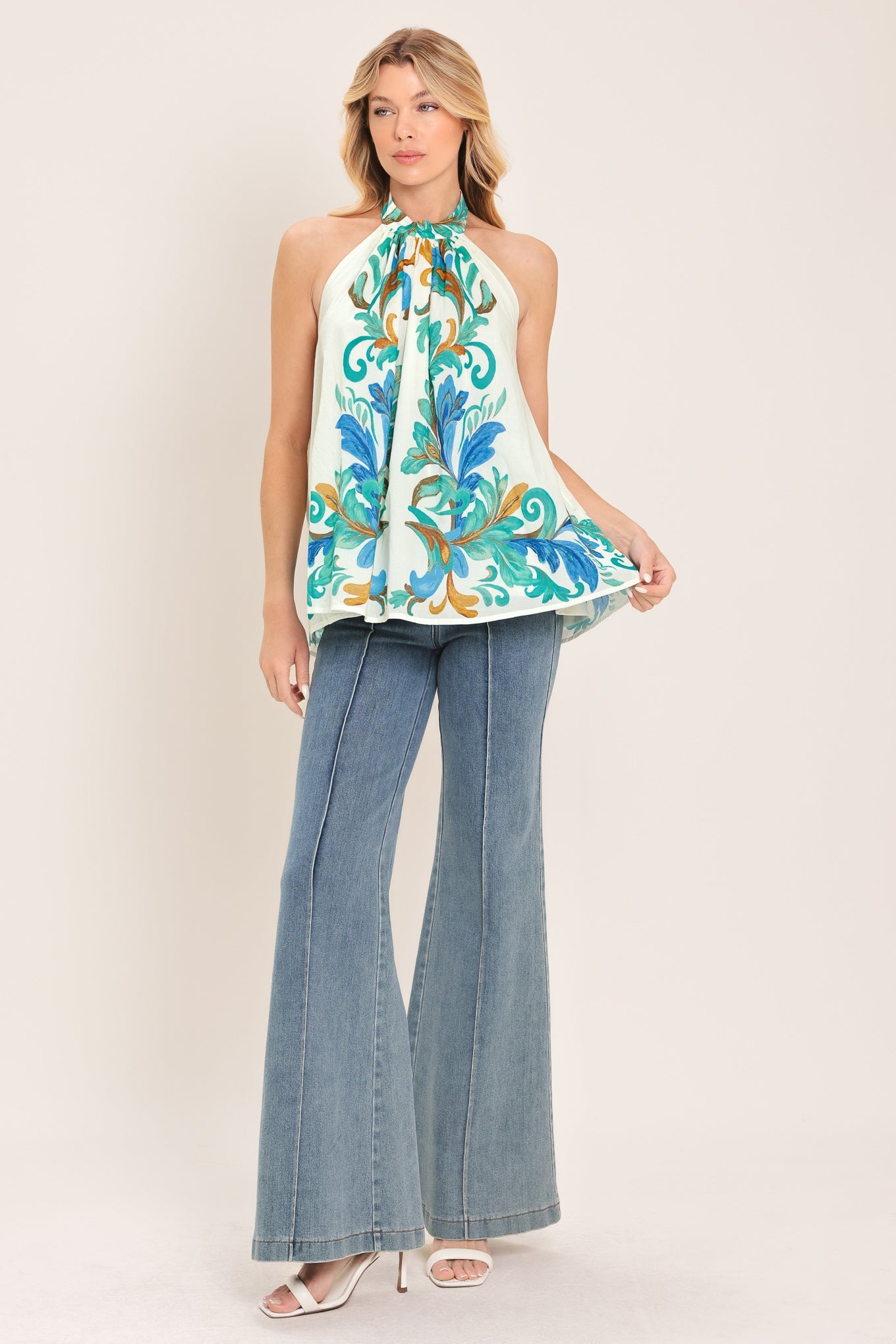 Woman wearing a sleeveless floral top and denim jeans on a white background
