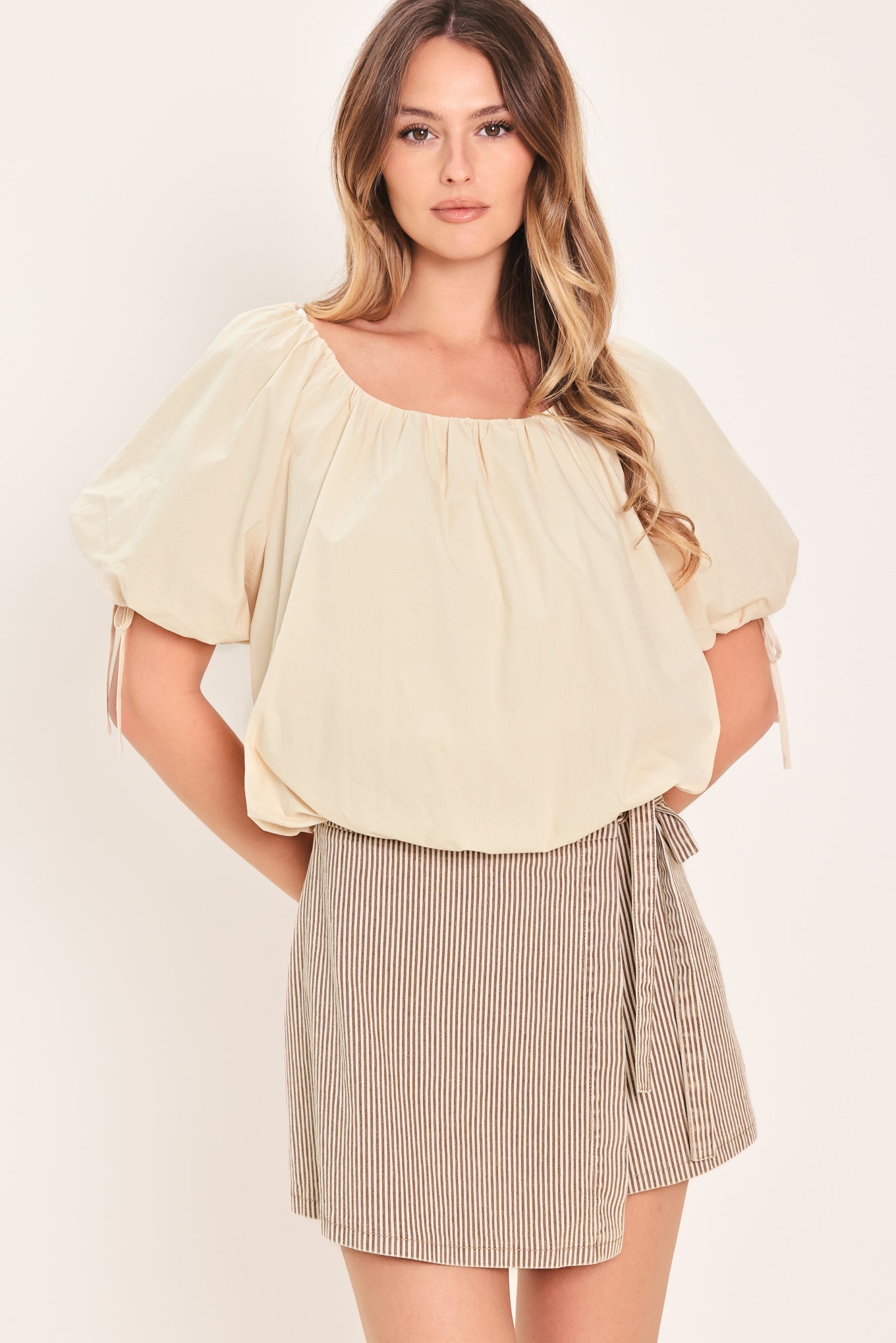 Woman wearing a light-colored blouse and striped skirt on a plain background