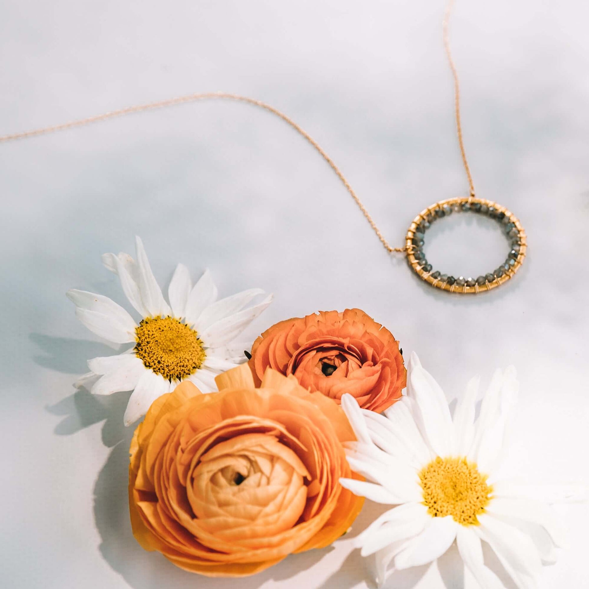 Necklace with a round pendant on a light gray background with flowers.