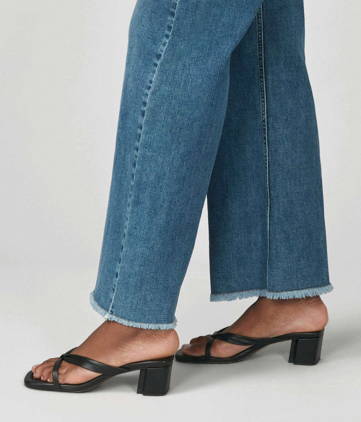 Person wearing blue jeans and black sandals on a plain background