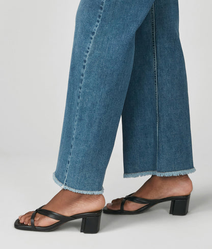 Person wearing blue jeans and black sandals on a plain background