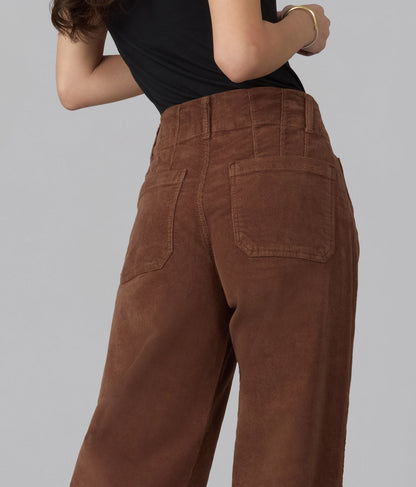A close-up back view of a person wearing high-waisted brown corduroy pants with a black top, set against a solid gray studio background.