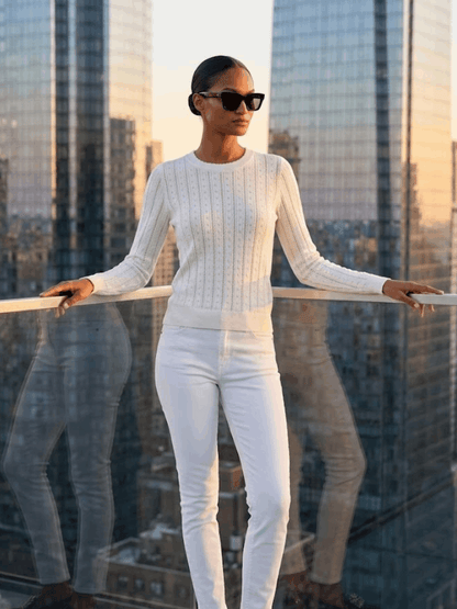 Model wearing a white pointelle knit sweater with a skyscraper background.