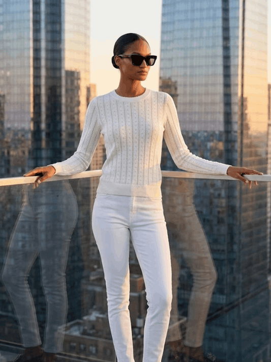 Model wearing a white pointelle knit sweater with a skyscraper background.