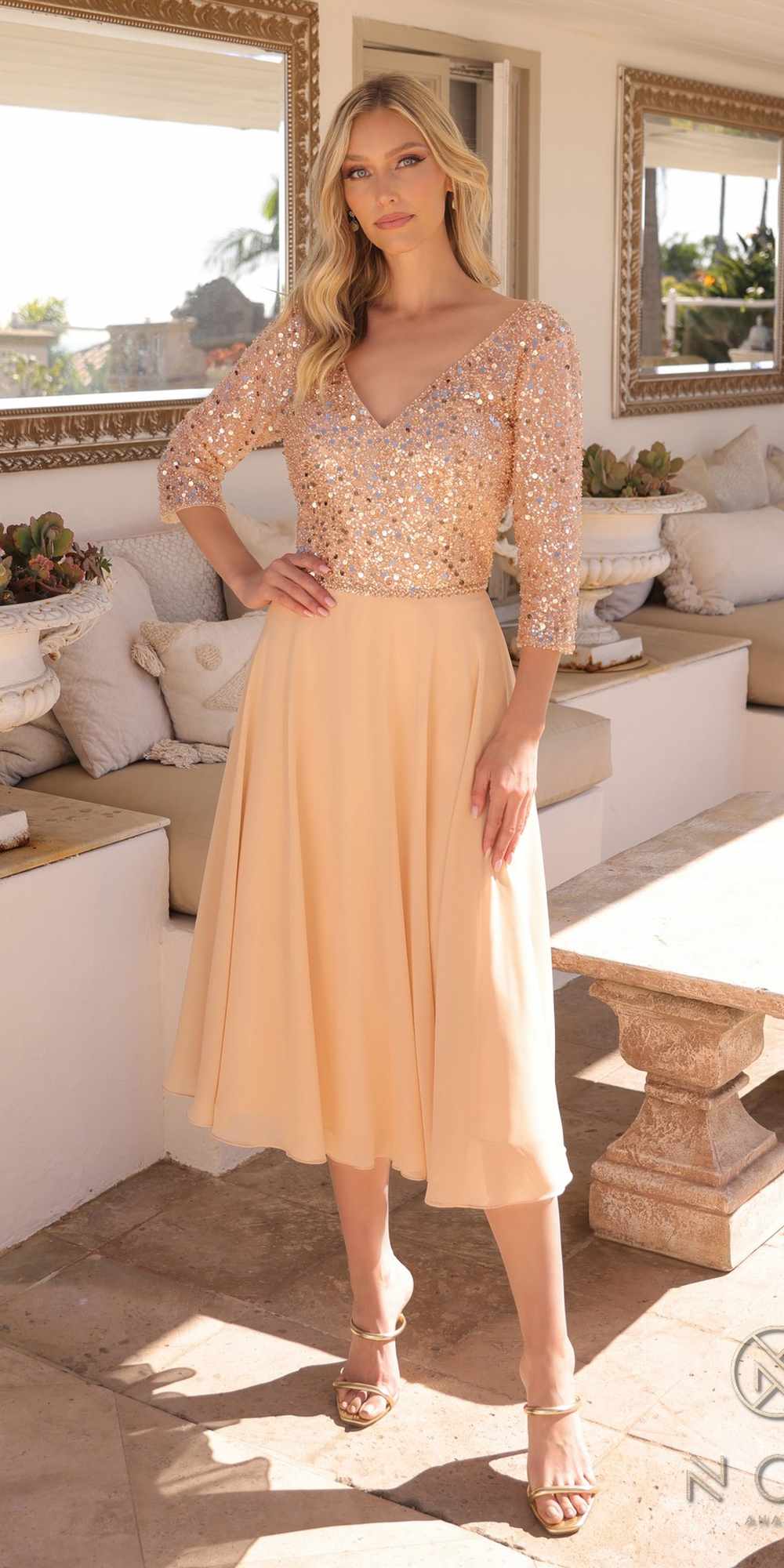 Woman in a peach dress with long sleeves standing in a sunlit room.