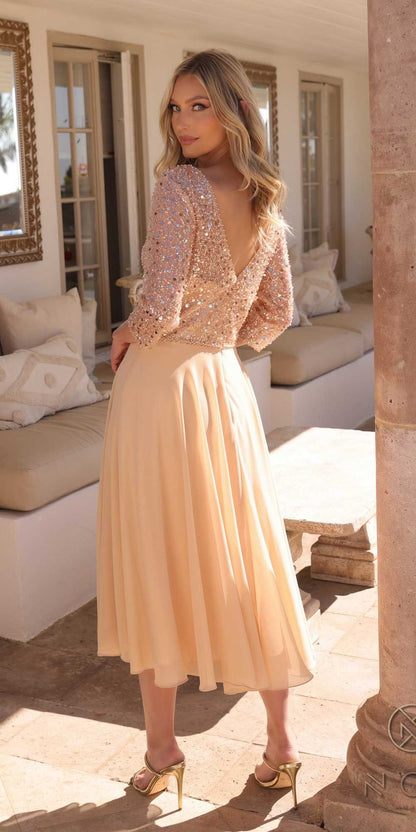 Woman in a beige dress standing in a sunlit room with large windows and a couch.