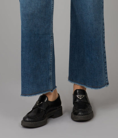 Black loafers worn with blue jeans on a gray background