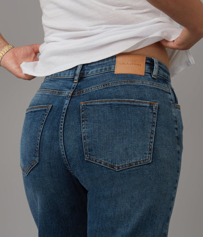 Person wearing blue jeans with a visible brand label on a gray background