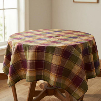 A round table covered with a plaid tablecloth in mustard yellow, burgundy, olive green, and beige.
