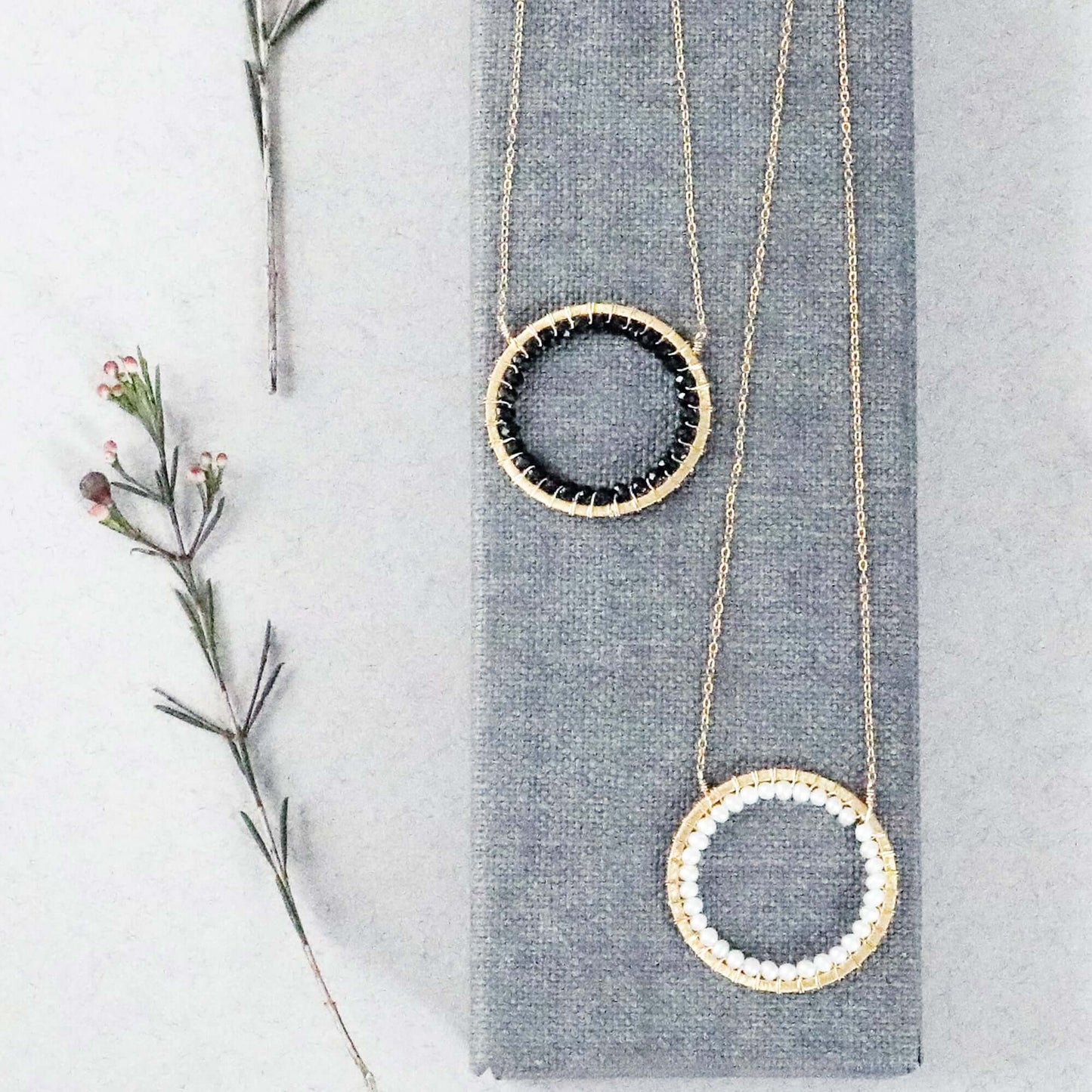 Two gold necklaces with circular pendants on a gray surface with a branch.