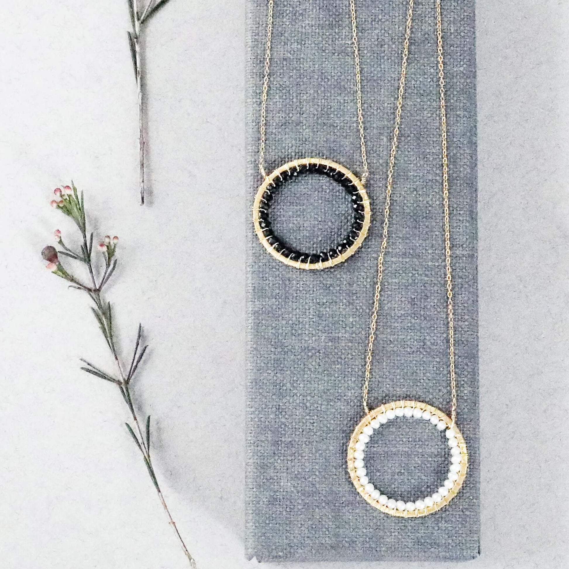 Two gold necklaces with circular pendants on a gray surface with a branch.