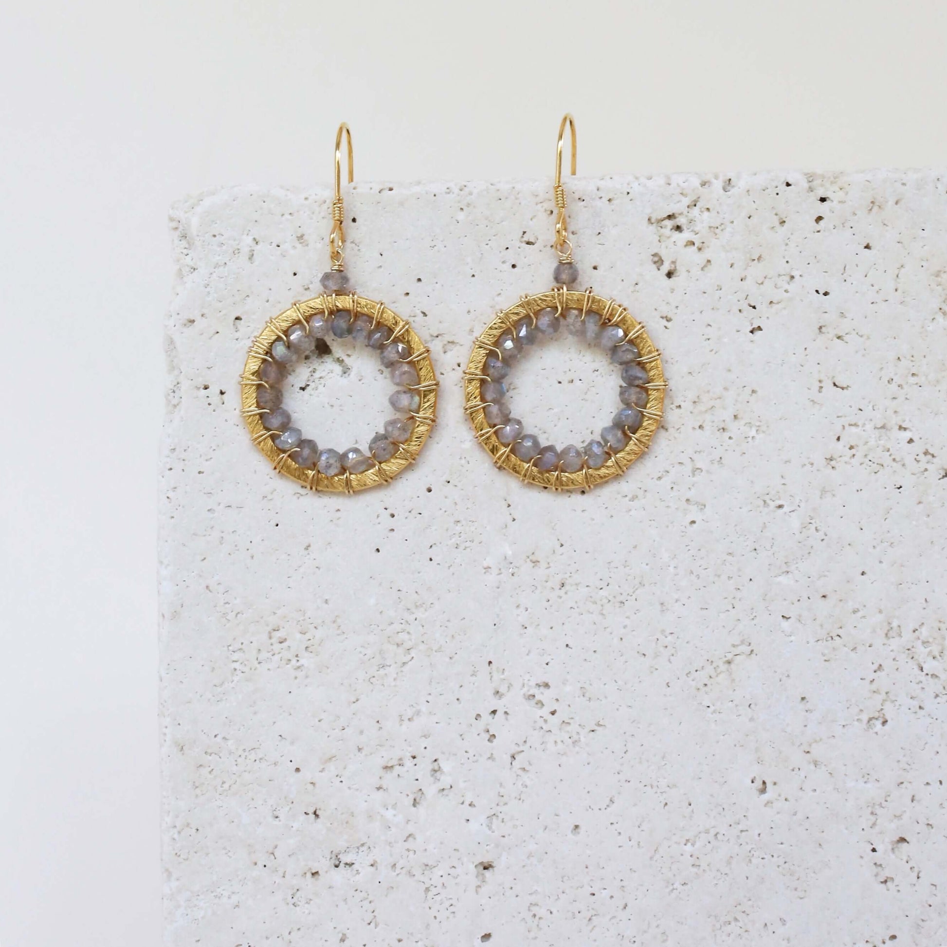 Gold hoop earrings with circular designs on a textured white surface