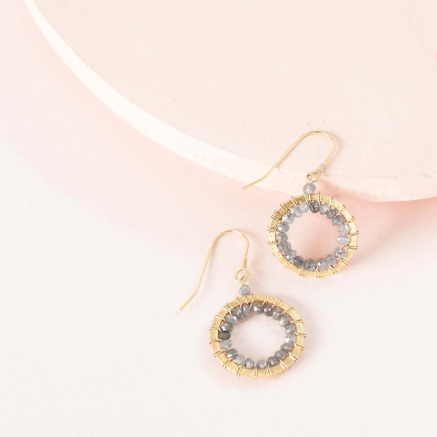 Gold and gray beaded earrings on a light pink background