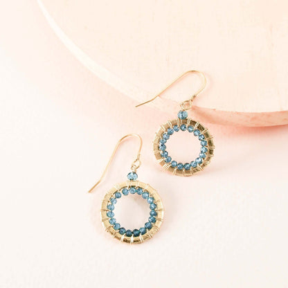 Gold hoop earrings with blue beads on a light pink background