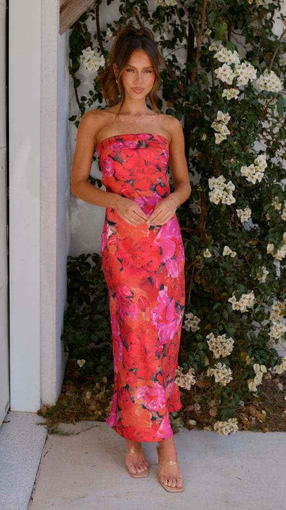 Satin strapless backless midi dress in vibrant pink with floral patterns, worn by a model against a floral backdrop.