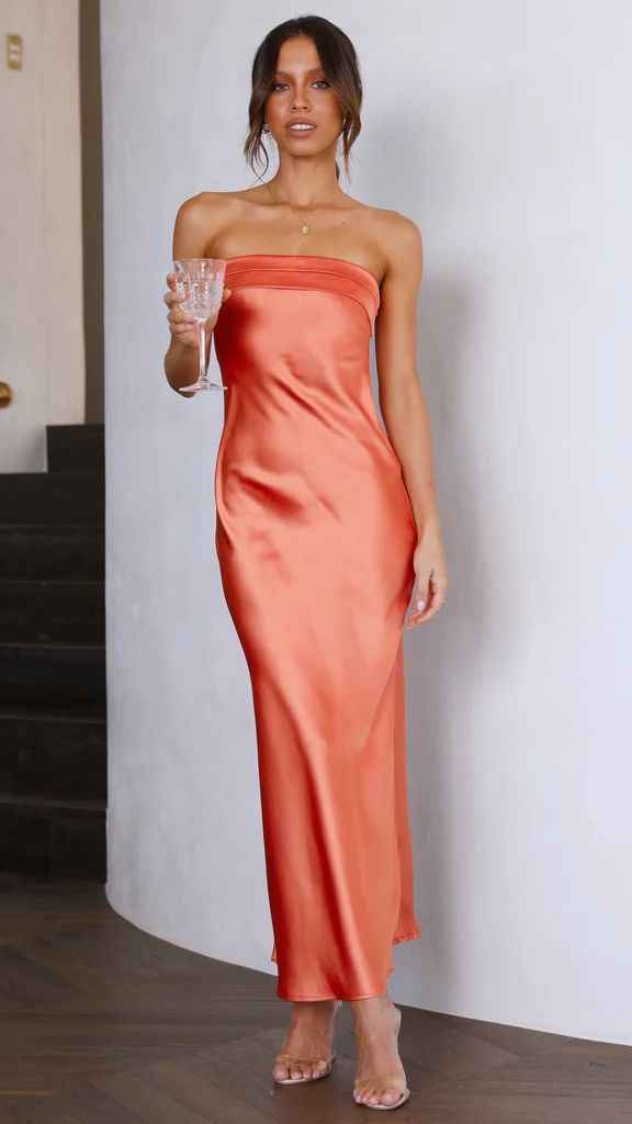 Satin strapless backless midi dress in orange, featuring a side slit, worn by a model holding a glass.