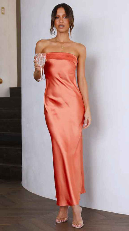 Satin strapless backless midi dress in orange, featuring a side slit, worn by a model holding a glass.