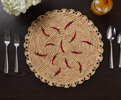 Scattered chili handwoven raffia round placemat with red chili designs, placed on a dark wooden table.