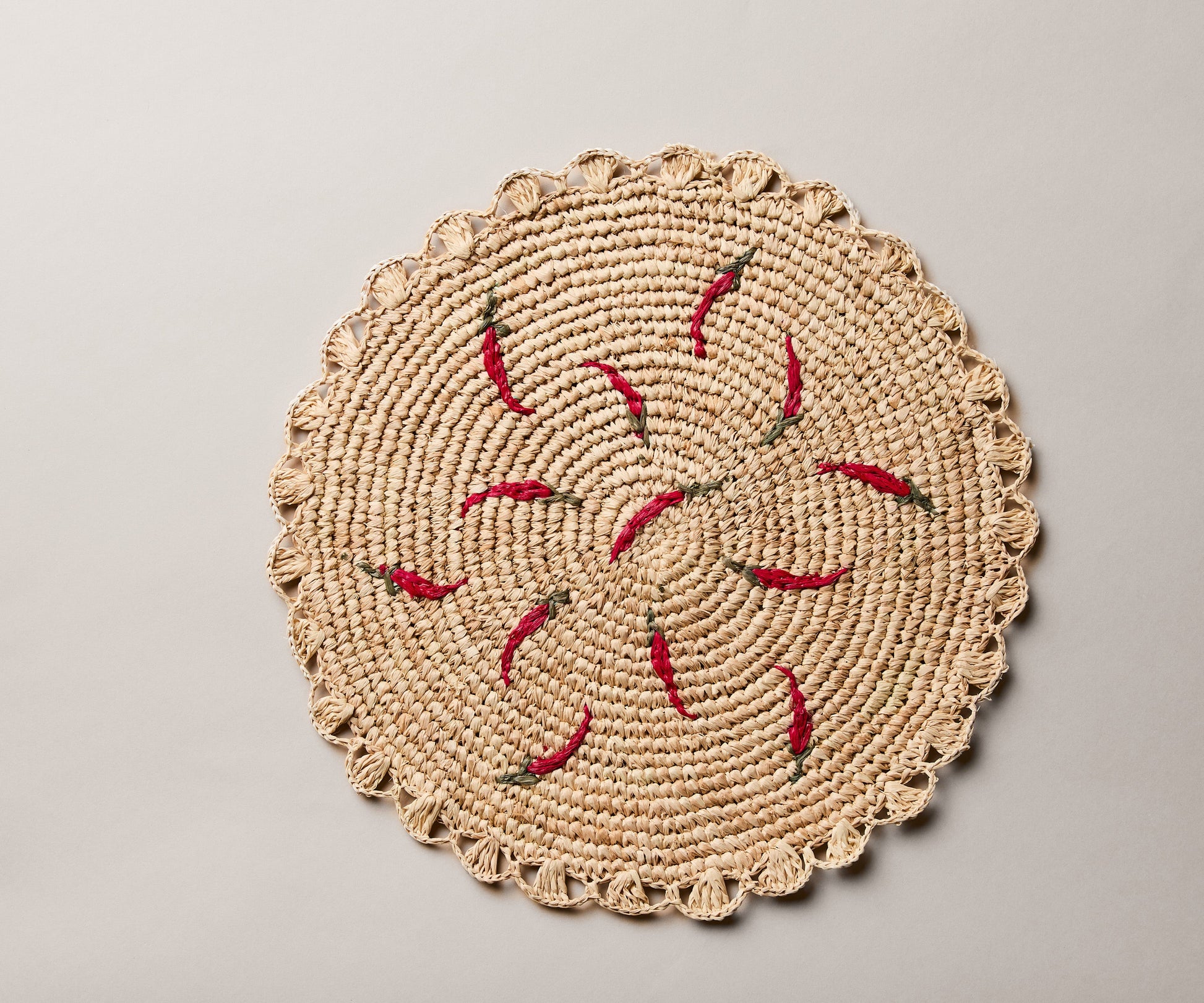 Scattered chili handwoven raffia round placemat with red chili pepper designs on a natural woven background.