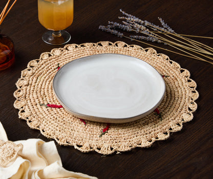 Scattered chili handwoven raffia round placemat with a beige color, featuring red chili accents and a white plate on top.