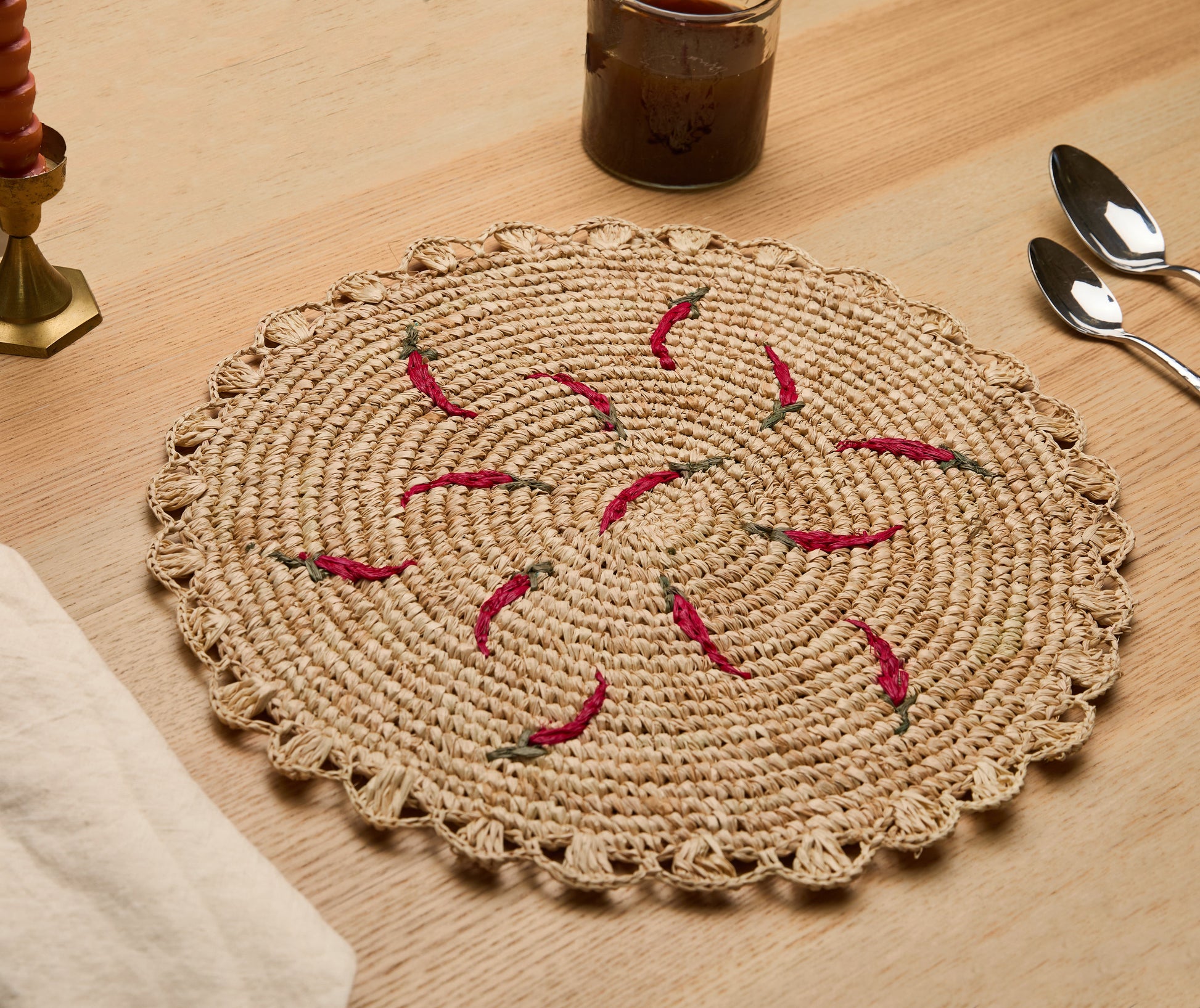 Scattered chili handwoven raffia round placemat with red chili designs on a natural woven background.