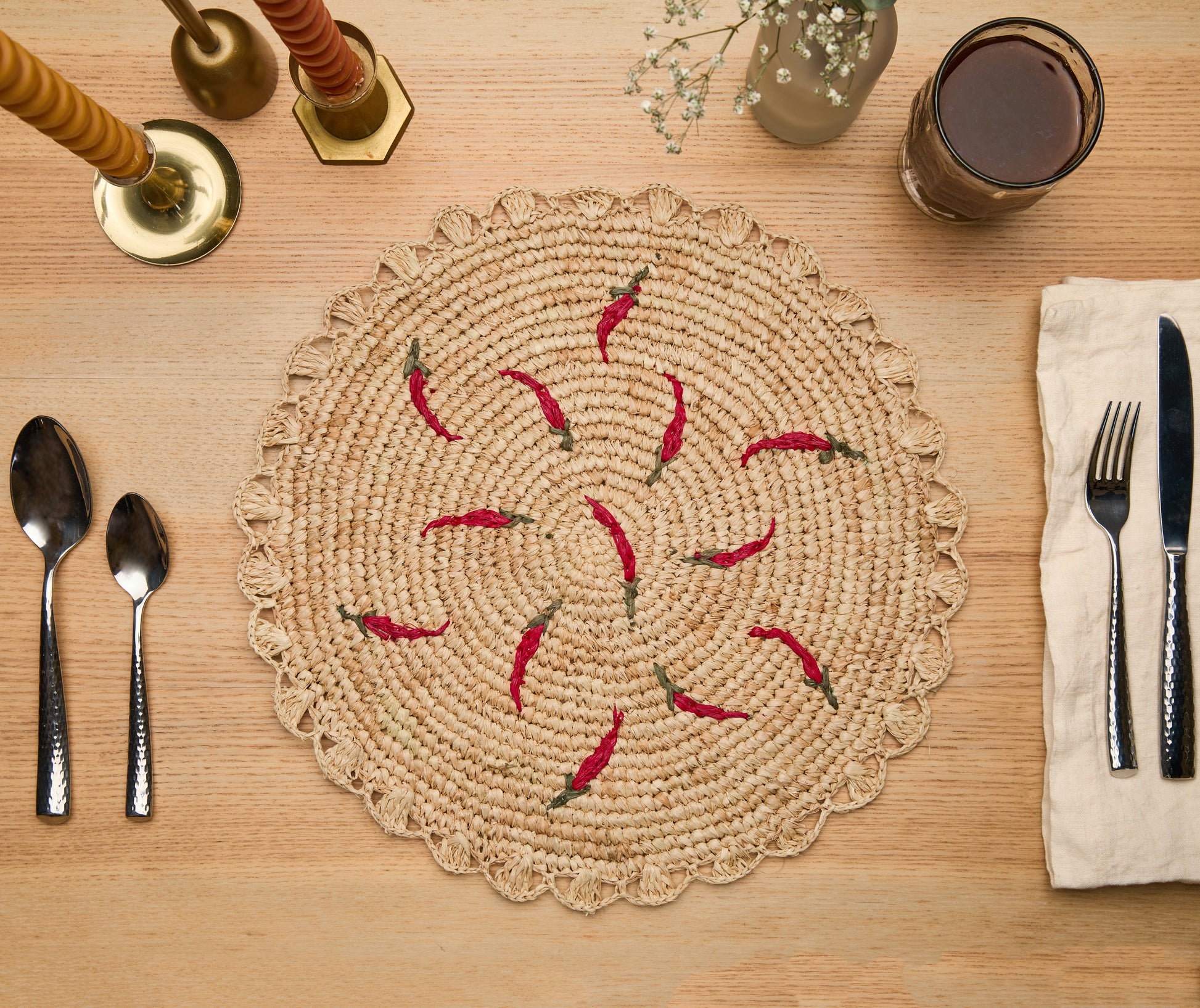 Scattered chili handwoven raffia round placemat with red chili designs on a wooden table setting.