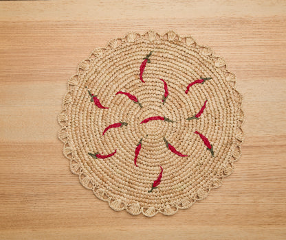 Scattered chili handwoven raffia round placemat with red chili pepper accents on a wooden surface.