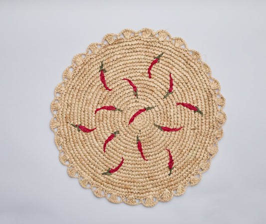 Scattered chili handwoven raffia round placemat with red chili pepper designs on a natural woven background.
