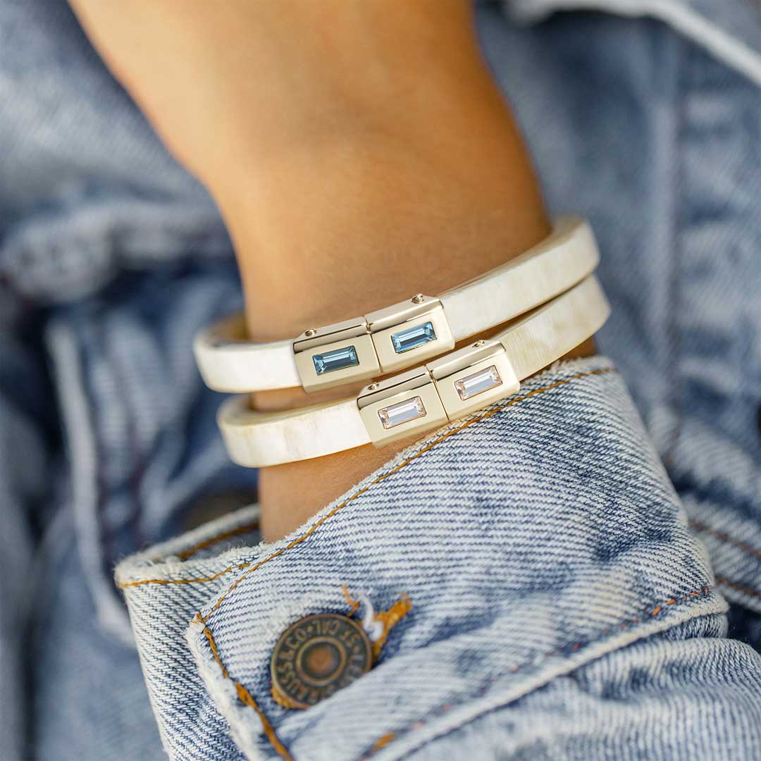Stack of gold bracelets with gemstones on a wrist against a denim background