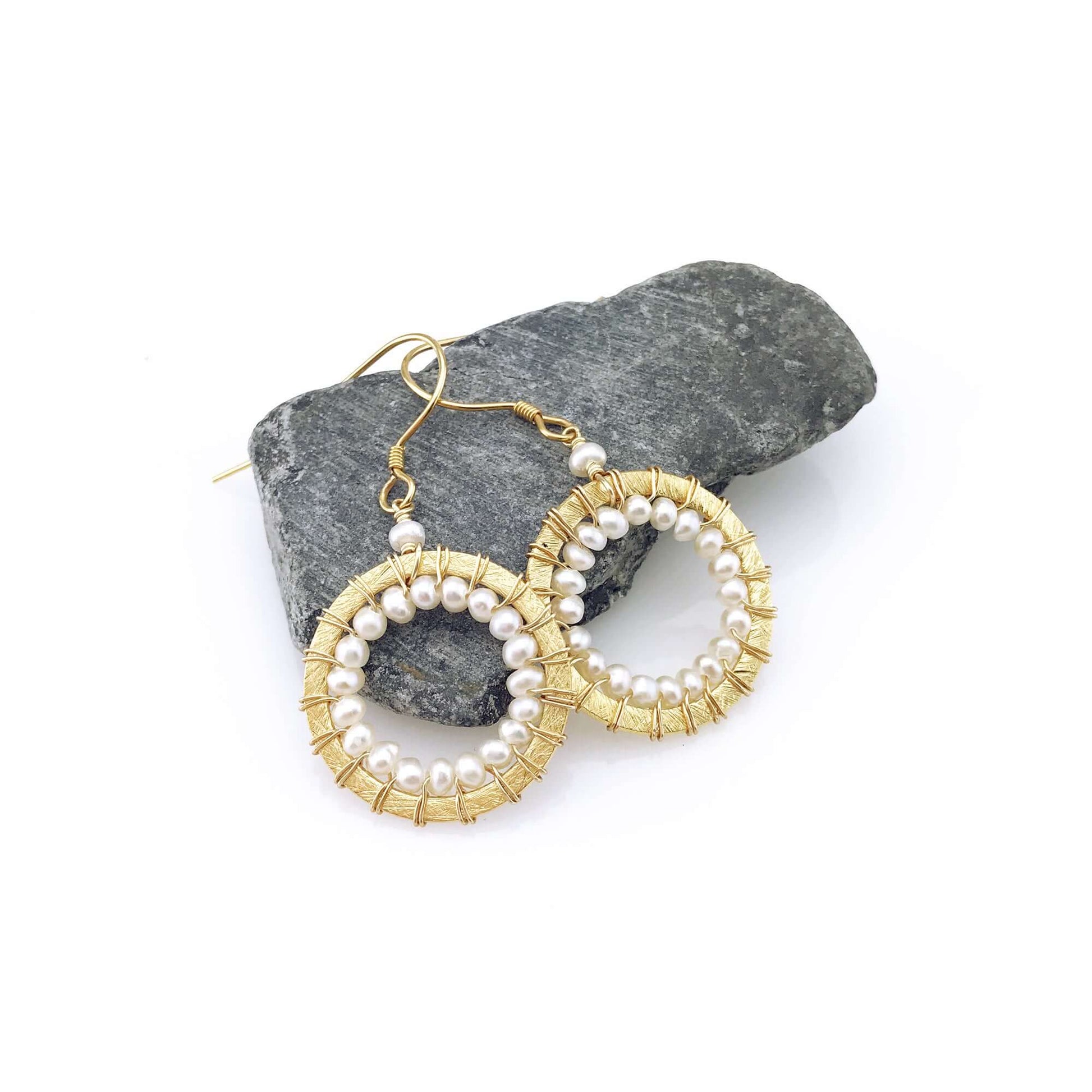 Gold and pearl earrings on a stone surface