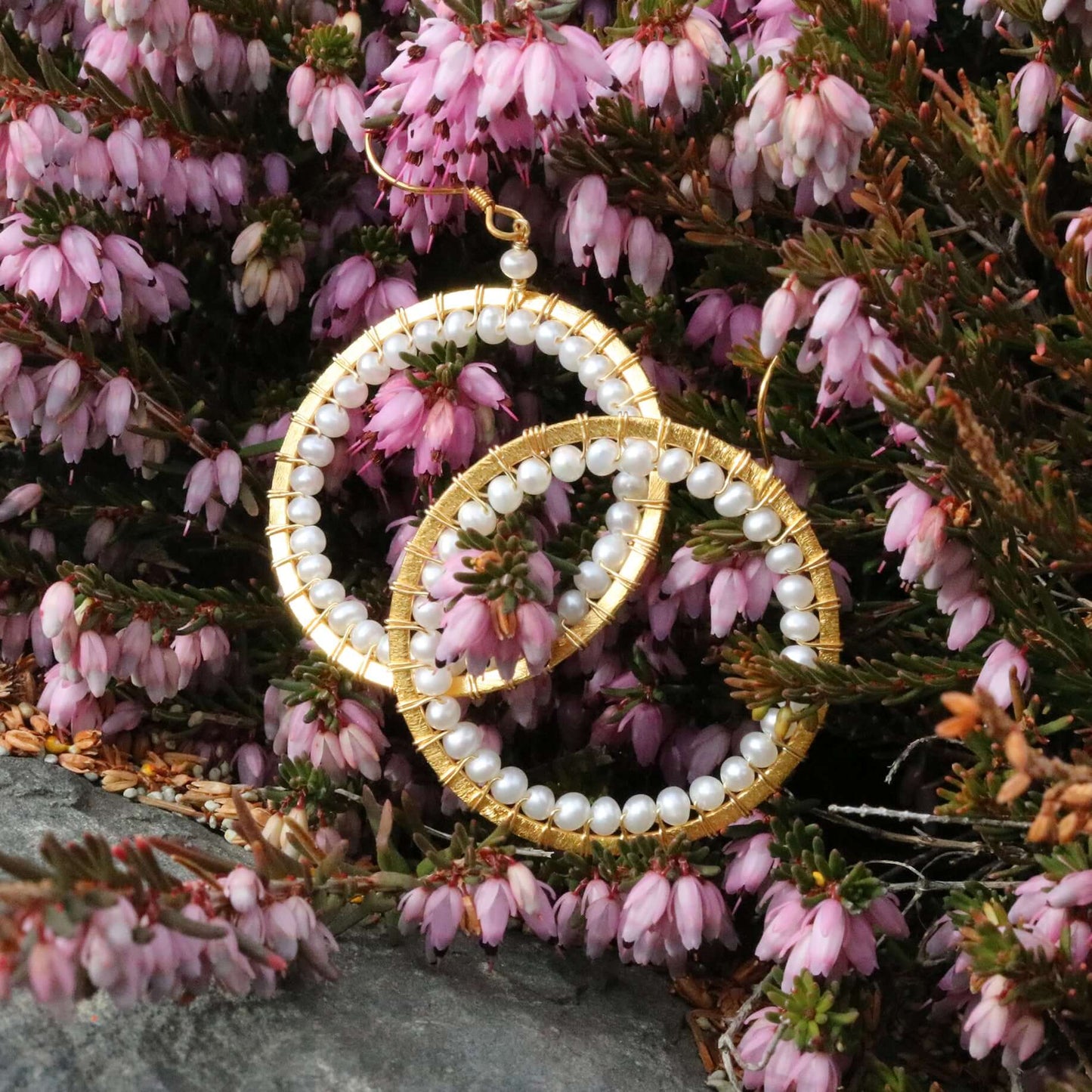 Gold and pearl hoop earrings on pink heather flowers