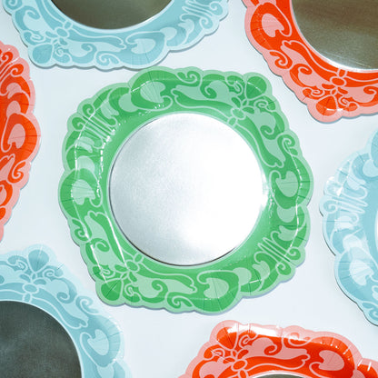 Seven scalloped paper plates in green, blue, and pink with silver centers and ornate scroll patterns.