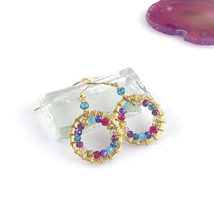 Multicolored beaded hoop earrings on a clear crystal surface with a purple stone in the background.