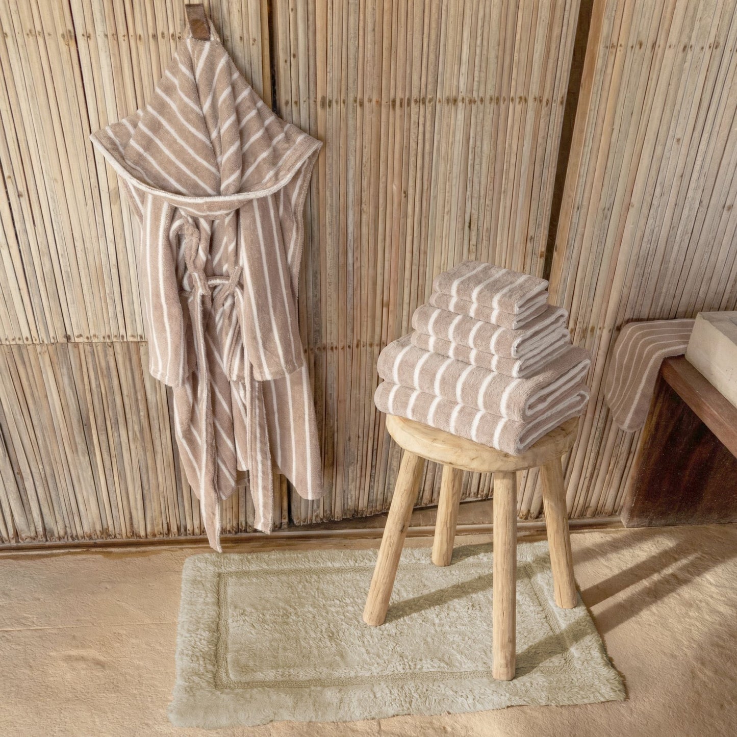 Striped robe and folded towels on a stool against a wooden paneled wall.