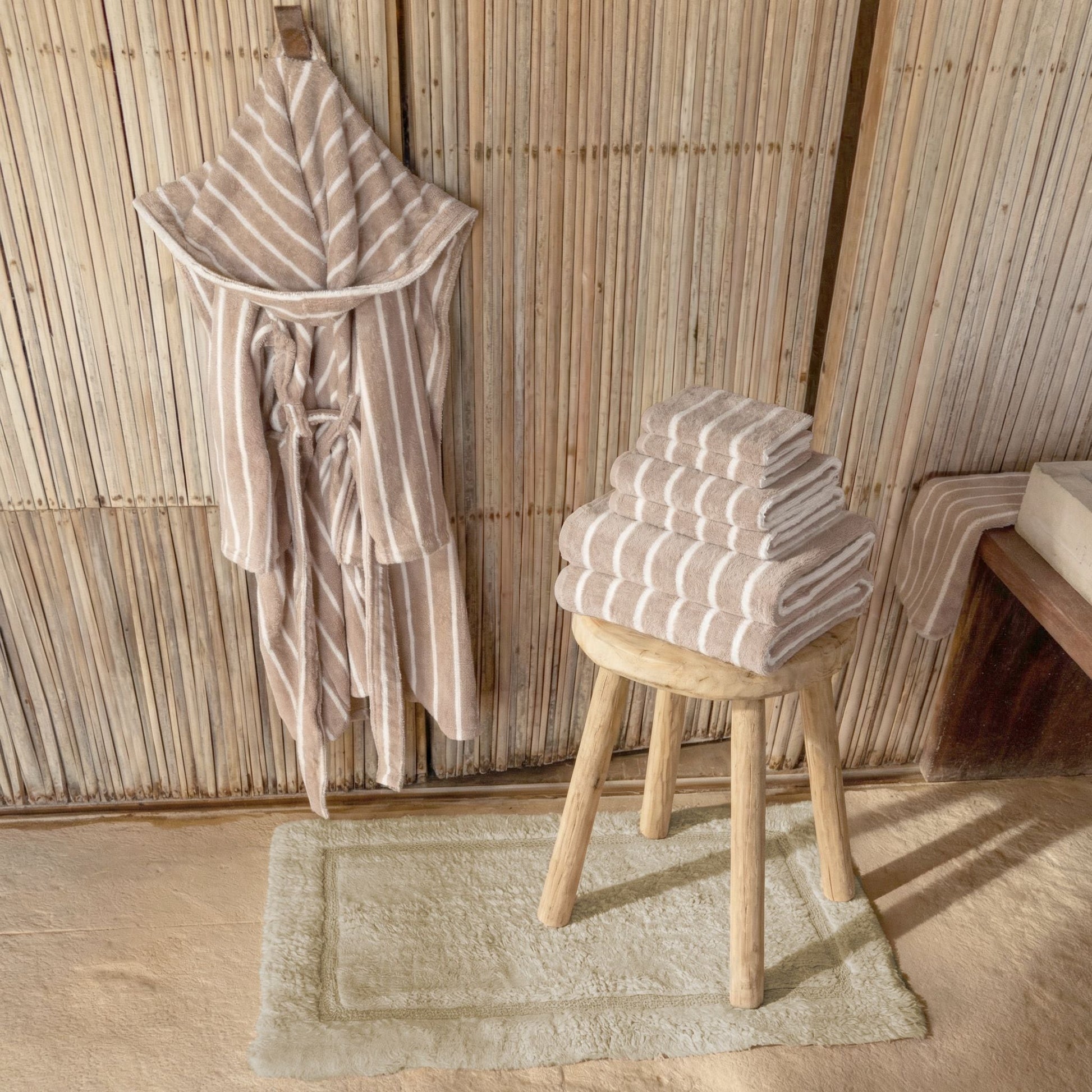 Striped robe and folded towels on a stool against a wooden paneled wall.