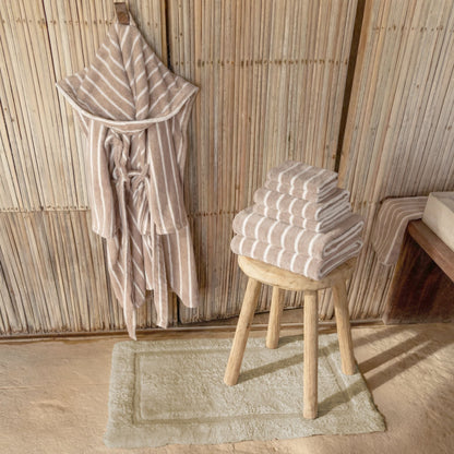 Striped robe and folded towels on a stool against a wooden paneled wall.
