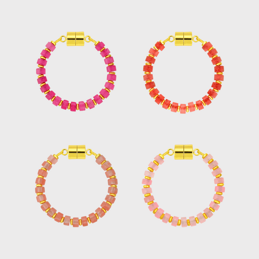 Four pairs of pink and red beaded hoop wine glass markers with gold accents on a light gray background.
