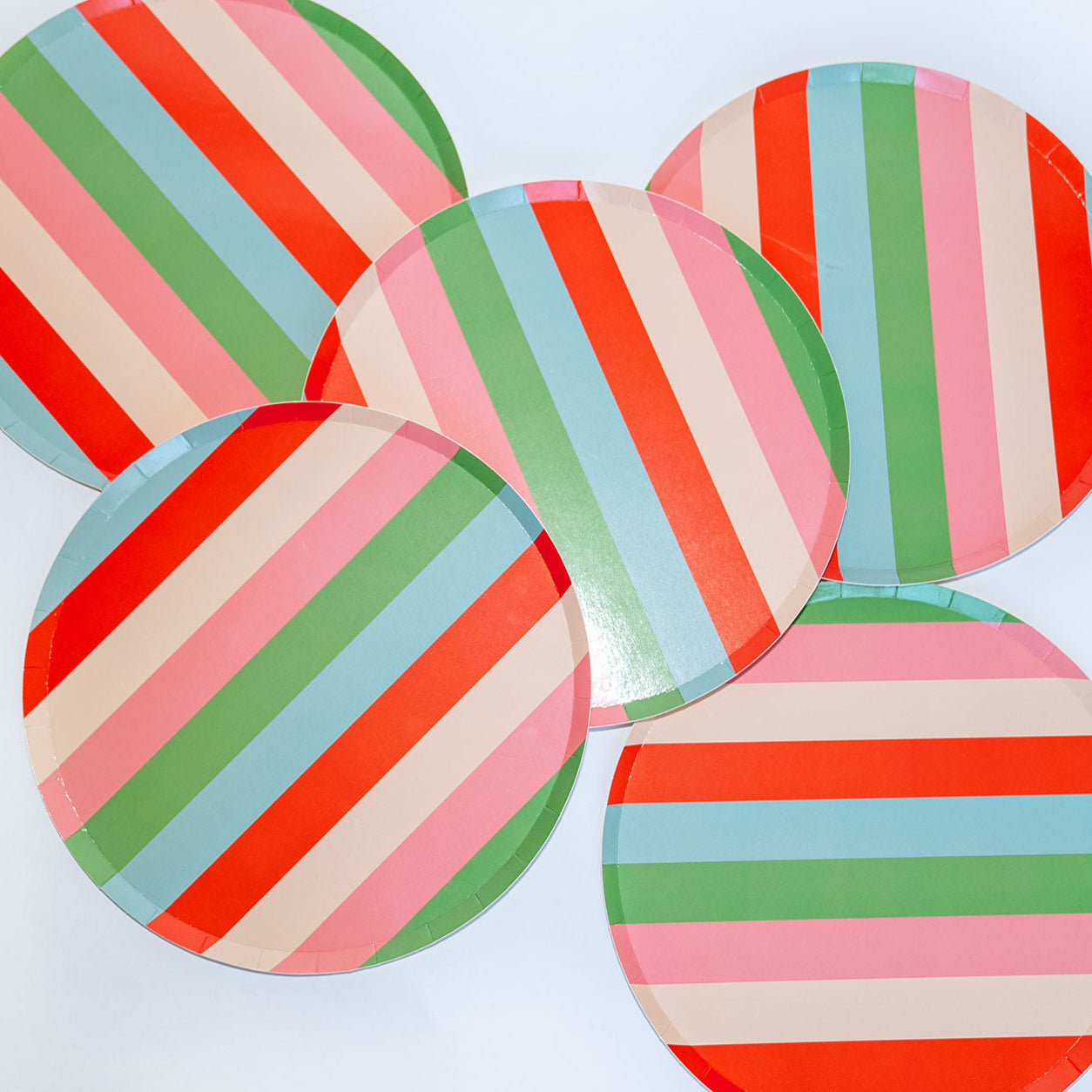 Five round paper plates with red, pink, green, and blue diagonal stripes arranged on a white surface.