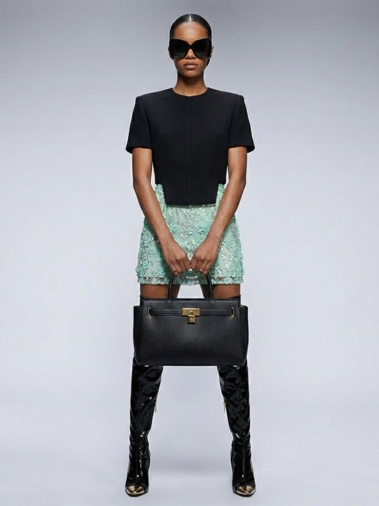 Front view of a light green mini skirt with floral embellishments, styled with a black top.