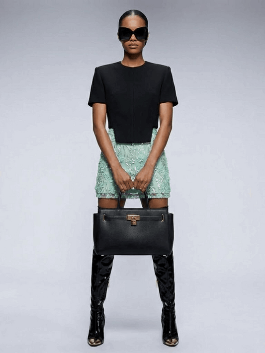 Front view of a light green mini skirt with floral embellishments, styled with a black top.