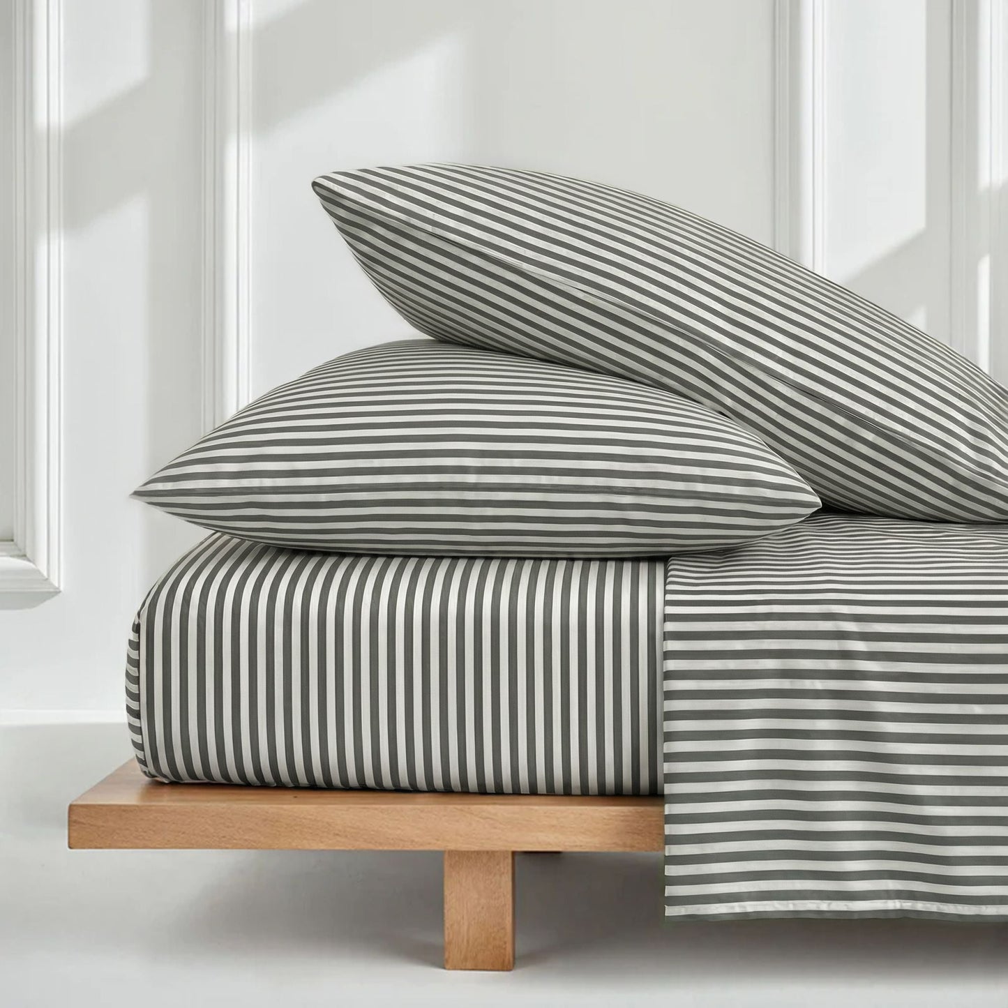 Striped bedding set on a wooden bed frame with white walls and windows in the background