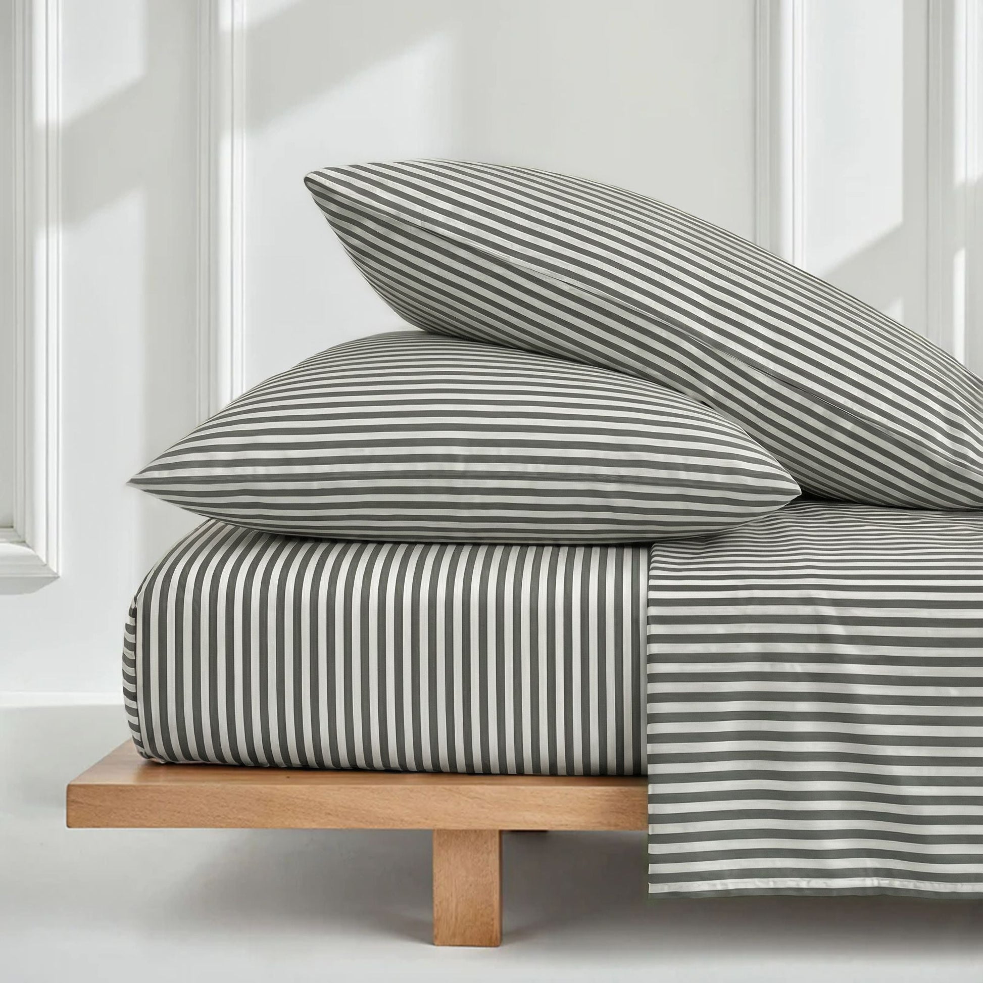 Striped bedding set on a wooden bed frame with white walls and windows in the background