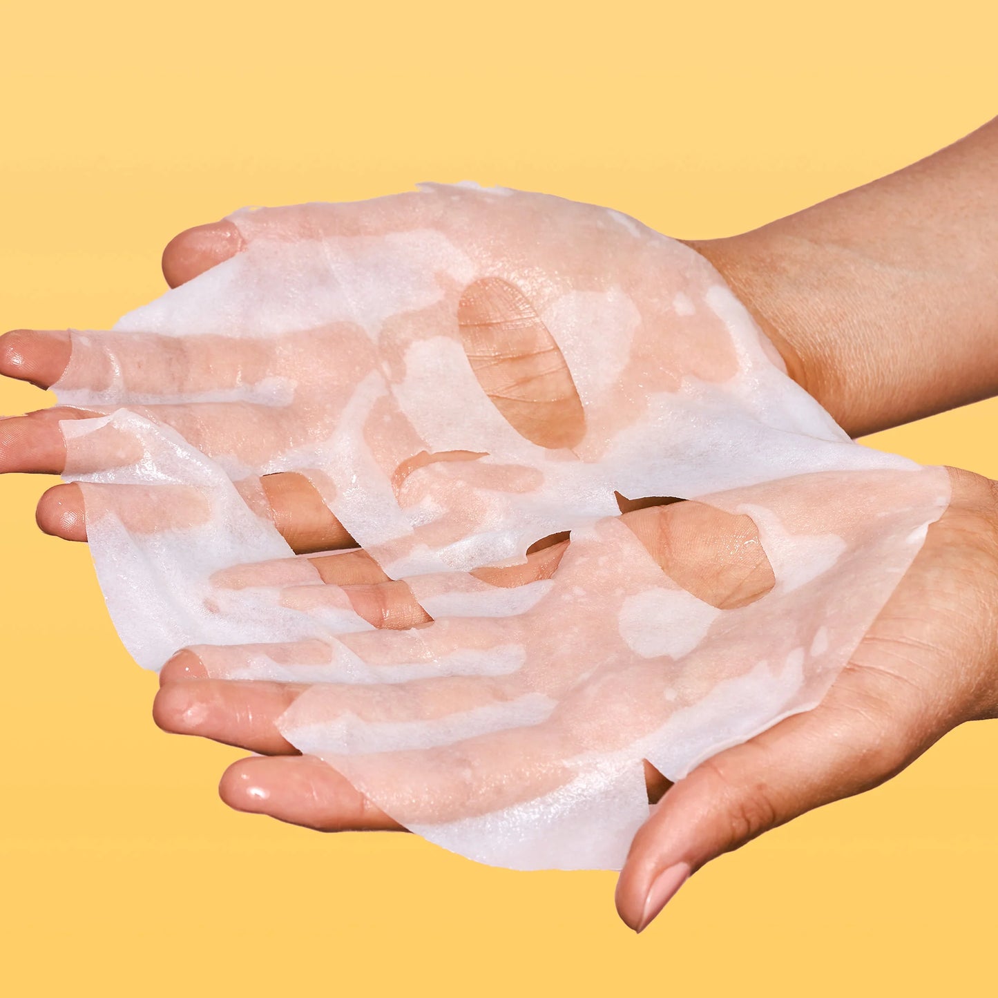 Hands holding a sheet mask against a yellow background