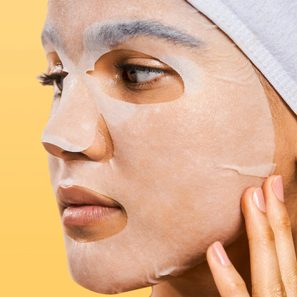 Person applying a face mask with a yellow background