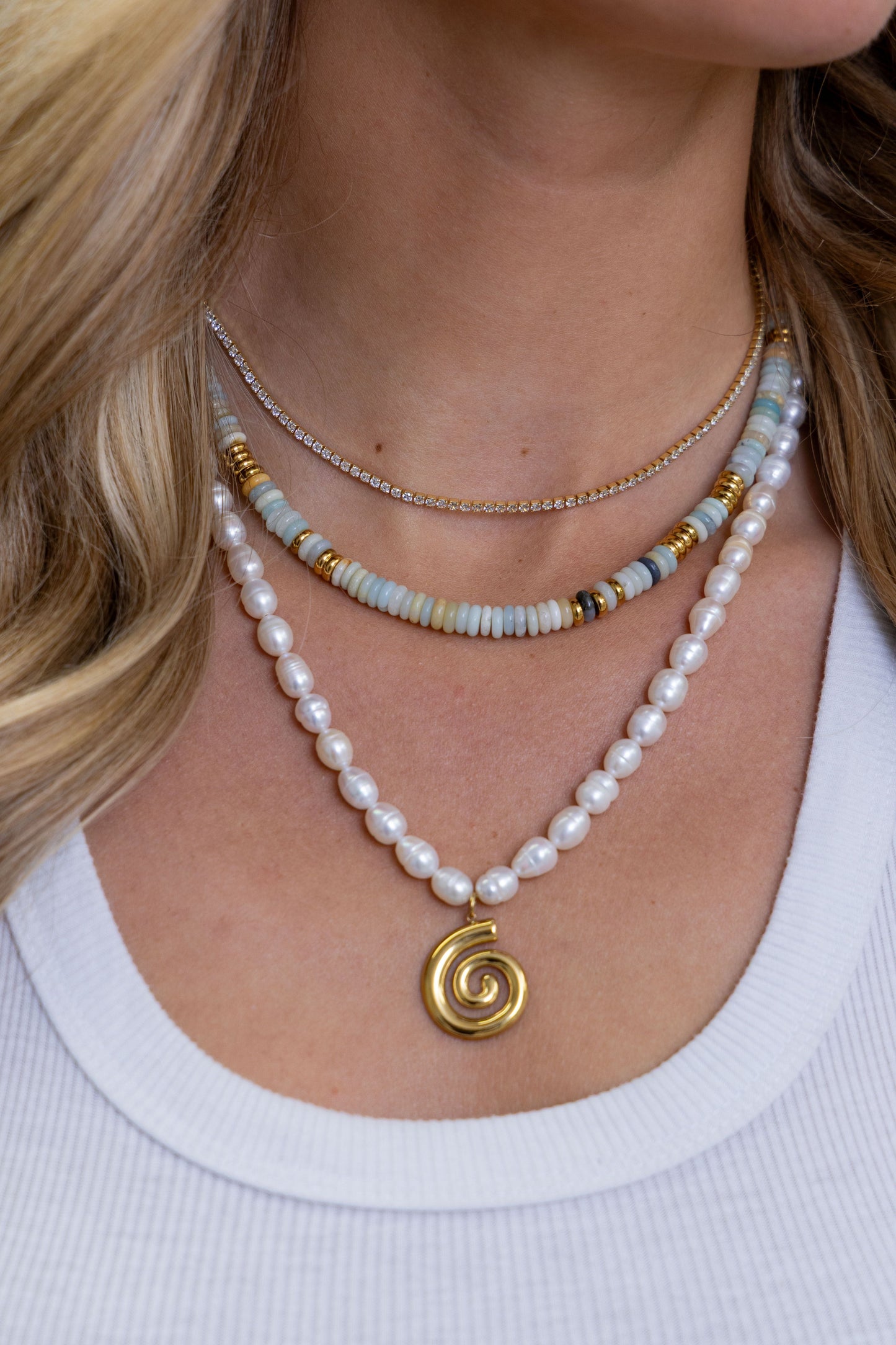 Close-up of a person wearing multiple necklaces with a focus on a gold spiral pendant.