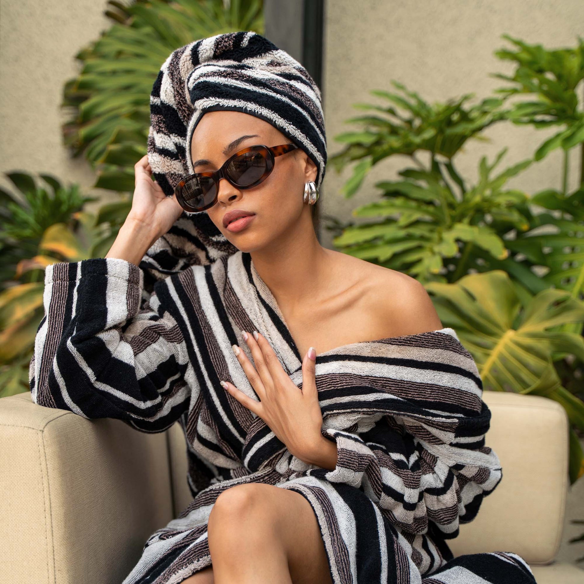 Woman in a striped robe and headscarf sitting on a couch with plants in the background