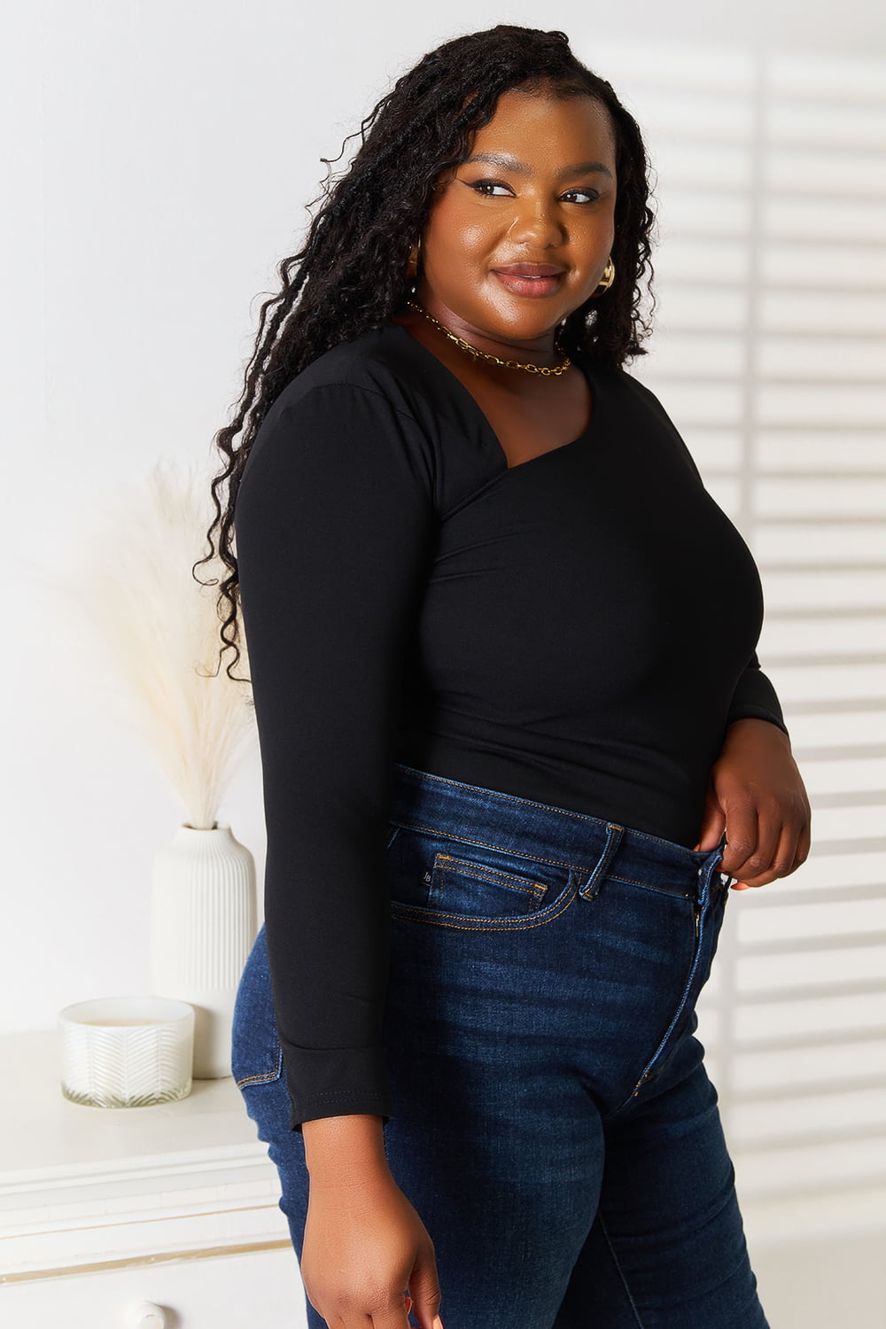 Woman wearing a black top and blue jeans standing indoors with a neutral background