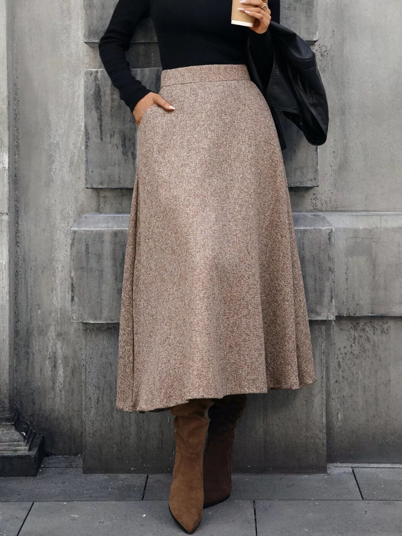 Person wearing a beige skirt and brown boots against a gray wall.